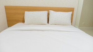 A bed with a wooden headboard, two pillows, and a white bedspread in a room with patterned wallpaper. - Minimalist 2BR Apartment at Parahyangan Residence (Bandung)