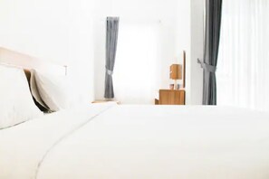 A modern hotel room with a large bed, a wooden nightstand, a small table, and a wardrobe. - Modern Style Studio at The Nest Puri Apartment (Tangerang)