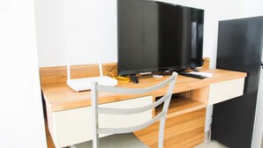 Uma mesa de madeira com monitor de computador, teclado e rato. Uma cadeira está posicionada em frente à mesa.