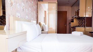 A modern bedroom with a large bed, a bedside table, a mirror, and a view into the kitchen area. - Modern Furnished Studio Room Cinere Bellevue Suites Apartment (Depok)