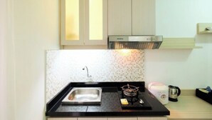 A compact kitchen with a sink, stove, and a microwave. - 1BR with Sofa Bed at Bassura City Apartment (Jakarta)