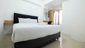 A modern bedroom with a large bed, a wooden headboard, and a small bedside table. - 1BR with Sofa Bed at Bassura City Apartment (Jakarta)