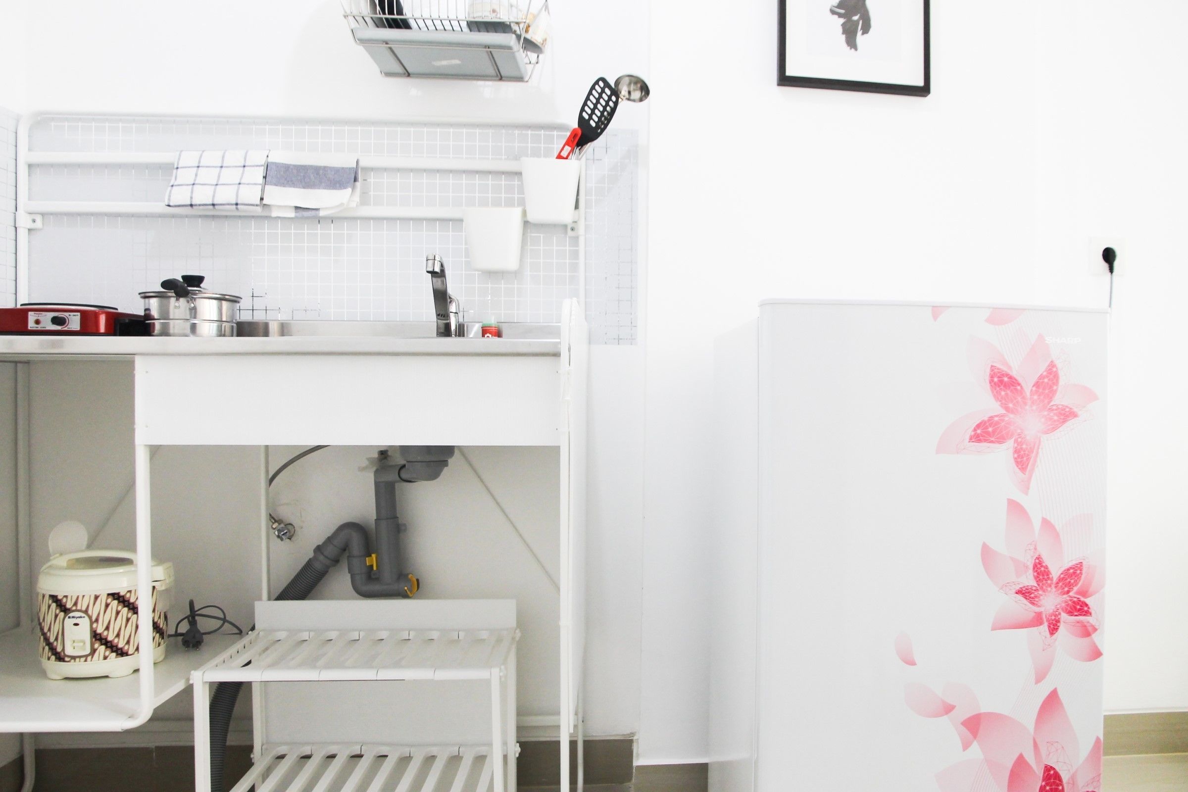 A kitchen with white cabinets, a sink, a stove, and a countertop with a kettle and a rice cooker.