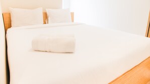A neatly made bed with white linens and a rolled towel, a wooden headboard, and a plain wall. - Simply Minimalist 2BR The Springlake Apartment (Bekasi)