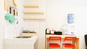 A kitchen with a sink, stove, and two red chairs. There are shelves above the counter and a water dispenser on the right. - Simply Minimalist 2BR The Springlake Apartment (Bekasi)