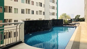 A swimming pool with a tiled edge, surrounded by a building with multiple balconies and windows. - Cozy 2BR Apartment with City View at Pavilion Permata (Surabaya)
