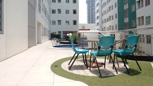 A rooftop terrace with a pool, outdoor seating, and high-rise buildings in the background. - Cozy 2BR Apartment with City View at Pavilion Permata (Surabaya)