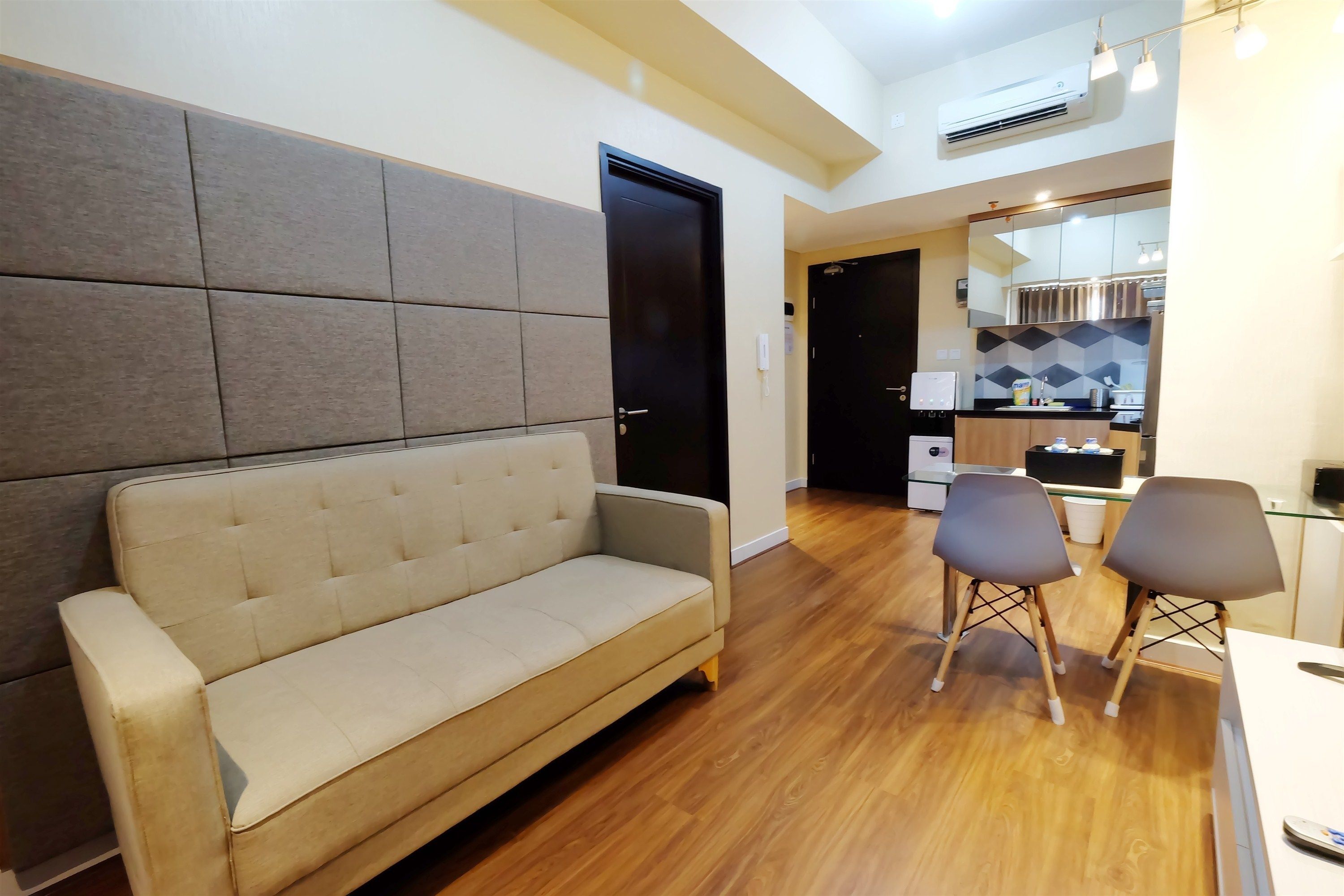 Un salon moderne avec un canapé, deux fauteuils, une table à manger et un coin cuisine à l’arrière-plan.