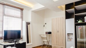 Quarto compacto com televisão, secretária pequena, cadeira, guarda-roupa e frigorífico.