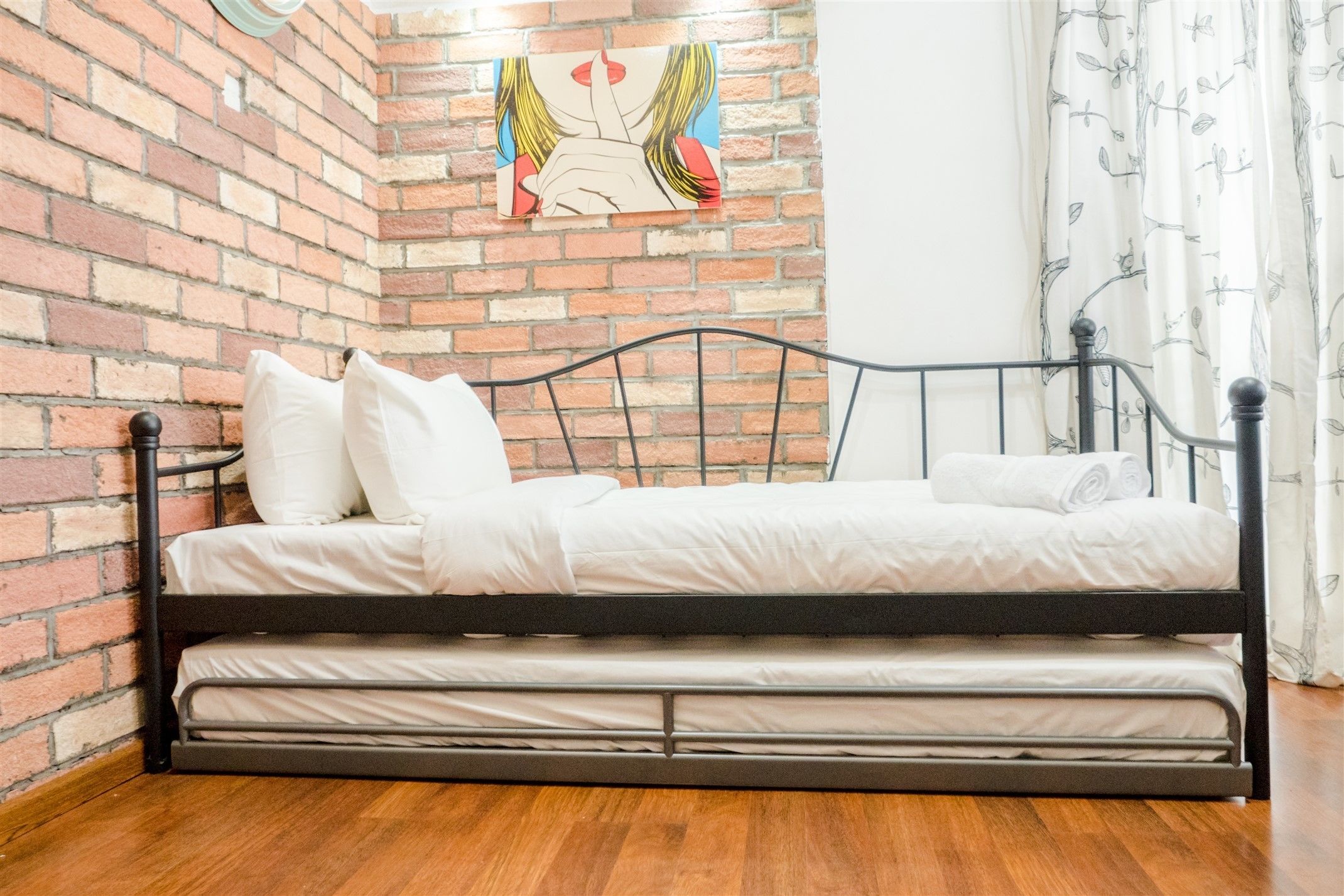 Een compact bed met metalen frame in een kamer met bakstenen muren en houten vloer.