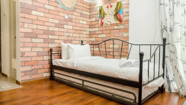 Uma cama de solteiro com estrutura metálica, roupa de cama branca e parede com padrão de tijolos.