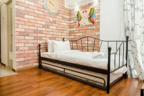 A single bed with a metal frame, white bedding, and a brick-patterned wall. - Cozy Studio Room The Jarrdin Cihampelas (Bandung)
