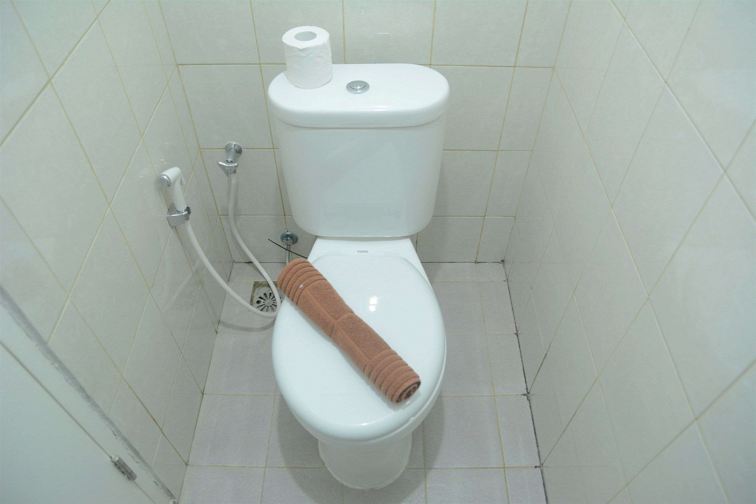 Des toilettes blanches, avec un rouleau de papier toilette posé sur le dessus et une serviette sur la lunette.