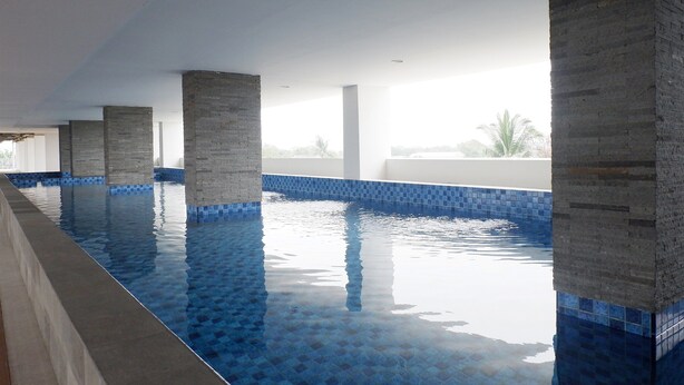 An indoor swimming pool with clear blue water, tiled walls, and concrete pillars. - Comfy Studio Poris 88 Apartment (Tangerang)