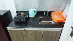 A kitchen with a gas stove, a kettle, a sink, and a dish rack. - Comfy Studio Poris 88 Apartment (Tangerang)