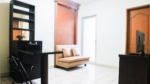 A living room with a sofa, a TV on a stand, a small table, and a chair. - 2BR Mediterania Palace Kemayoran Apartment (Jakarta)
