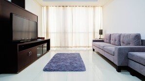 A modern living room with a flat-screen TV on a dark wooden cabinet, a grey sofa, and a blue rug on a tiled floor. - Luxurious Furnished 2BR Kemang Village Apartment (Jakarta)