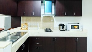 A modern kitchen with dark brown cabinets, a stainless steel sink, a microwave, and a gas stove. - Luxurious Furnished 2BR Kemang Village Apartment (Jakarta)