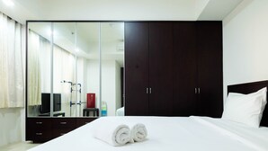 A hotel room with a large dark wooden wardrobe, a mirrored wardrobe, a neatly made bed with white linens, and a television on a stand. - Luxurious Furnished 2BR Kemang Village Apartment (Jakarta)