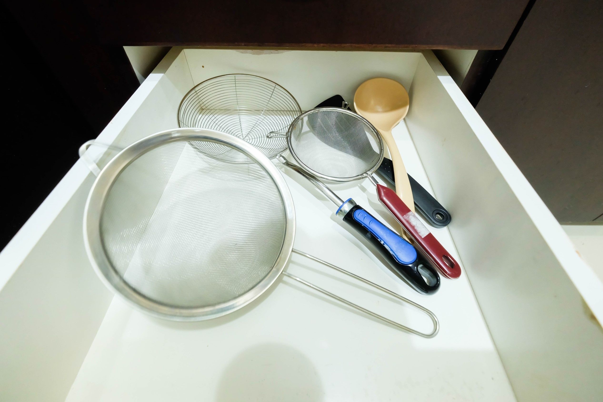 Un cajón con utensilios de cocina, como un colador, un tamiz y una espumadera.