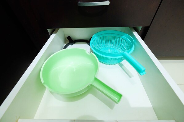 A kitchen drawer containing a green frying pan, a black spatula, and a blue colander.