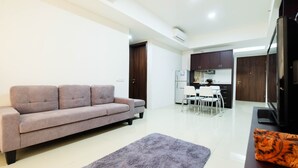 A modern living room with a sofa, a rug, and a kitchen in the background. - Luxurious Furnished 2BR Kemang Village Apartment (Jakarta)