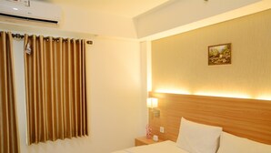 A hotel room with a bed, a nightstand, a lamp, a painting on the wall, and an air conditioning unit. - Simply Studio Room @ Annora Living Apartement Tangerang (Tangerang)