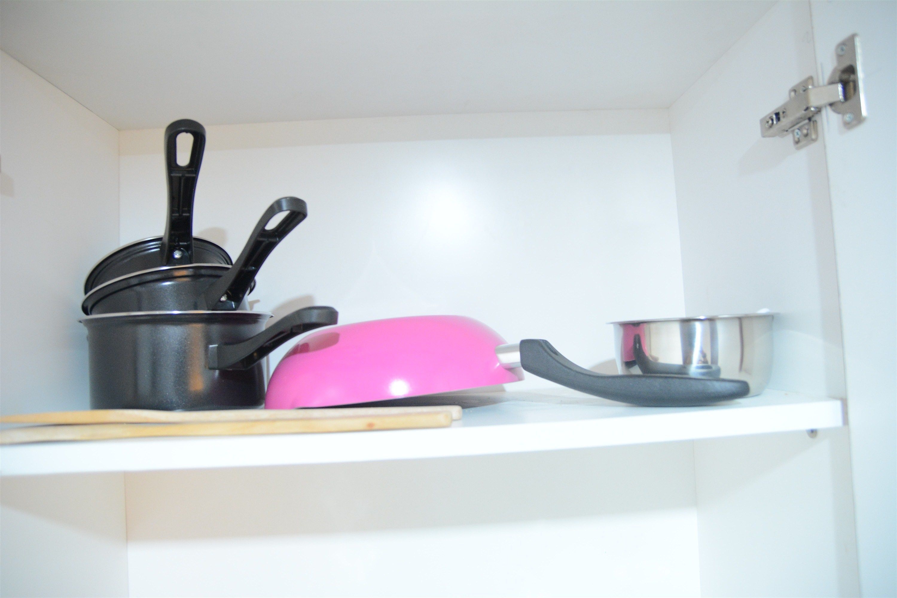 Une étagère de cuisine avec un pot, une spatule rose et un saladier en métal.