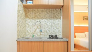 A compact kitchenette with a sink, a stove, and wooden cabinets. - Simply Studio Room @ Annora Living Apartement Tangerang (Tangerang)