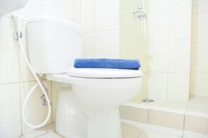 A white toilet with a blue tissue on the seat, a visible toilet paper holder, and a shower area with a glass door. - Comfortable 2BR Springlake Summarecon Apartment (Bekasi)