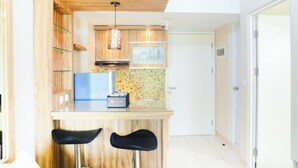 A compact kitchen with wooden cabinets, a built-in stove, and a small bar area with two stools. - Comfortable 2BR Springlake Summarecon Apartment (Bekasi)