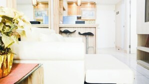A modern hotel room with a white sofa, a small table with a vase, and a view of the kitchen area. - Comfortable 2BR Springlake Summarecon Apartment (Bekasi)