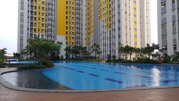 A swimming pool surrounded by greenery and tall residential buildings with balconies. - Comfortable 2BR Springlake Summarecon Apartment (Bekasi)