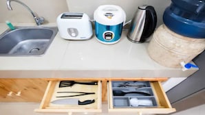 A kitchen with a sink, toaster, kettle, and a water dispenser. There is a drawer with utensils and a container. - Homey Studio Room The Nest Apartment (Tangerang)