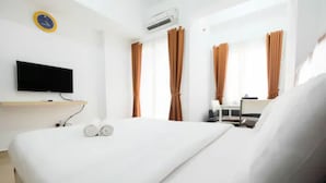 A hotel room with a bed, a TV on a stand, an air conditioner, and curtains. - Homey Studio Room The Nest Apartment (Tangerang)