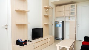 A compact living space with a TV, a refrigerator, a dining table, and a small kitchen area. - Comfortable 2BR Parahyangan Residence Apartment (Bandung)