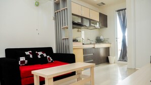A modern living room with a black sofa, a red throw blanket, and a wooden coffee table. - Comfortable 2BR Parahyangan Residence Apartment (Bandung)