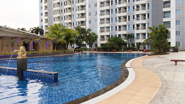 Une piscine agrémentée d’une fontaine décorative, entourée d’une terrasse carrelée et de palmiers.