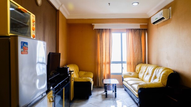 Un espacio habitable compacto con refrigerador, sofá, una mesita y una ventana con cortinas.