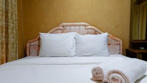Una cama bien hecha con sábanas y almohadas blancas, una toalla enrollada al lado y un cabecero de madera.
