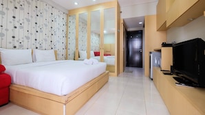 A hotel room with a large bed, a TV, a minibar, and a wardrobe with mirrors. - Central Jakarta Studio Apartment At Tamansari Sudirman (Jakarta)