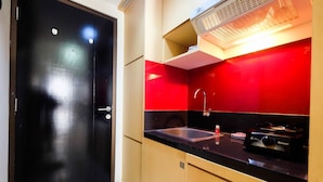 A compact kitchen with a black door, a red backsplash, a sink, and a stove. - Central Jakarta Studio Apartment At Tamansari Sudirman (Jakarta)