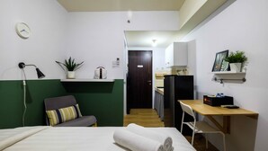 A hotel room with a bed, a desk, a chair, a small table, a plant, a clock, and a mirror. - Bright Studio Apartment Serpong Greenview (South Tangerang)