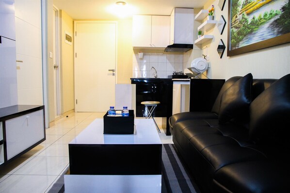 A modern living room with a black leather sofa, a white coffee table, and a kitchen area with white cabinets and a black stove.