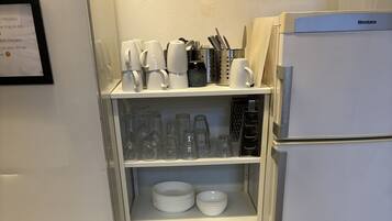 Ett kök med ett vitt kylskåp, hyllor med tallrikar, koppar och glas.