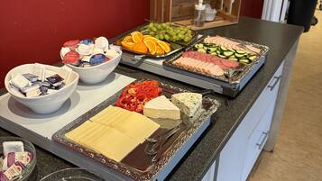 En buffet med forskellige spiser, herunder ost, kød, frugt og grøntsager.