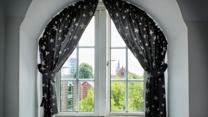 A window with star-patterned curtains, a white frame, and a view of buildings and trees outside.