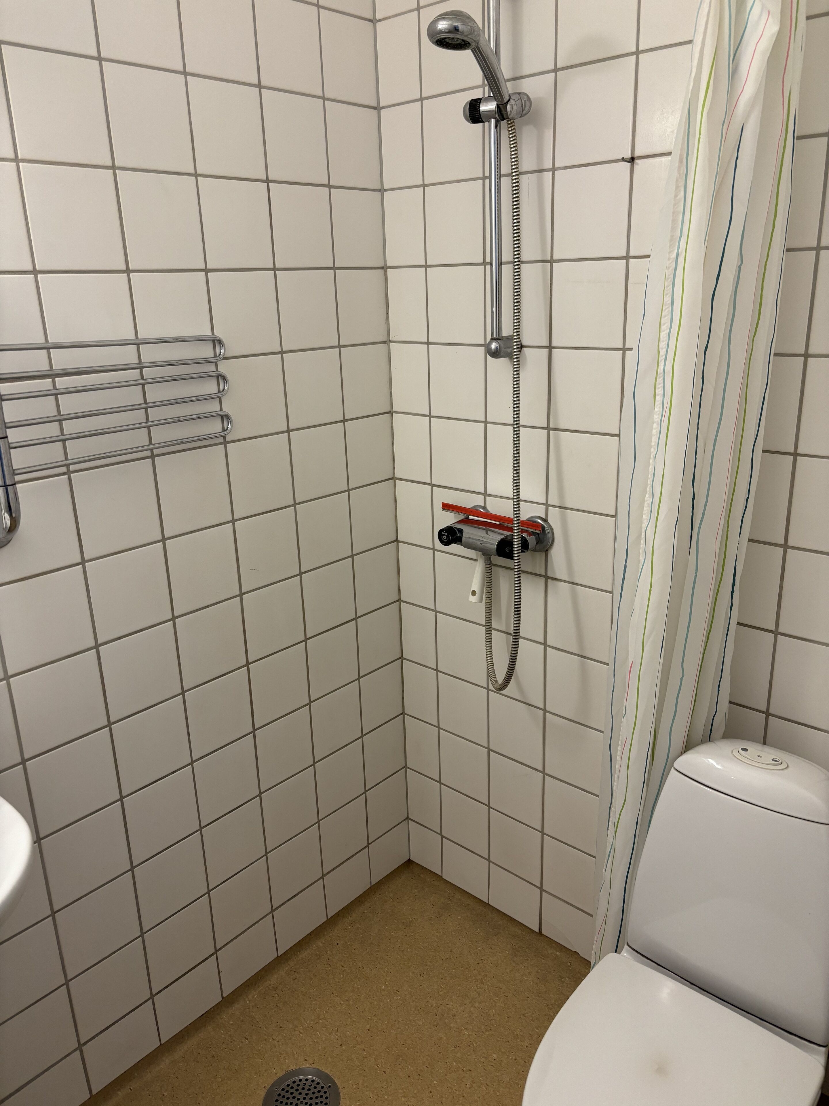 Et lille badeværelse med fliser, en bruser, toilet og et håndklædetørrestativ.
