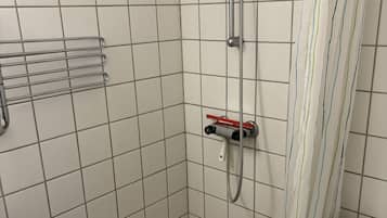 Et lille badeværelse med fliser, en bruser, toilet og et håndklædetørrestativ.