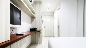 Une chambre d’hôtel avec un lit, un téléviseur fixé au mur, une table de chevet en bois et une porte donnant sur une autre pièce.